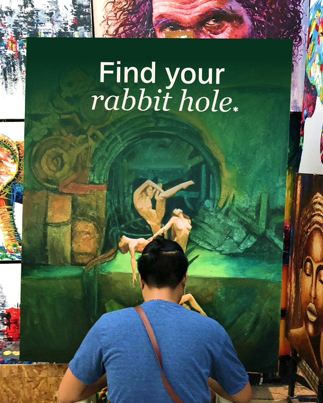 Man painting large green canvas with phrase at top find your rabbit hole